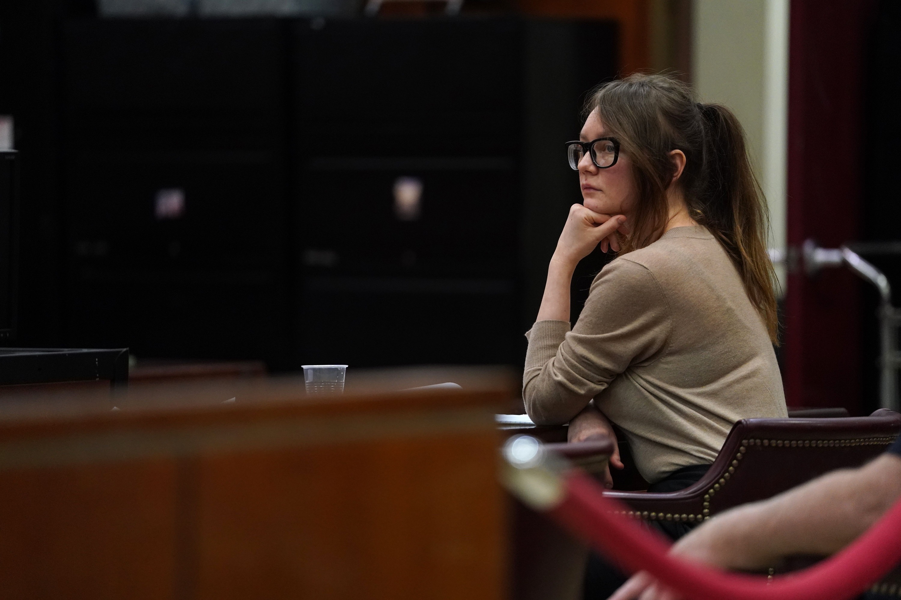 Anna Sorokin (aka Anna Delvey) sits in a courtroom leaning her chin on her hand.