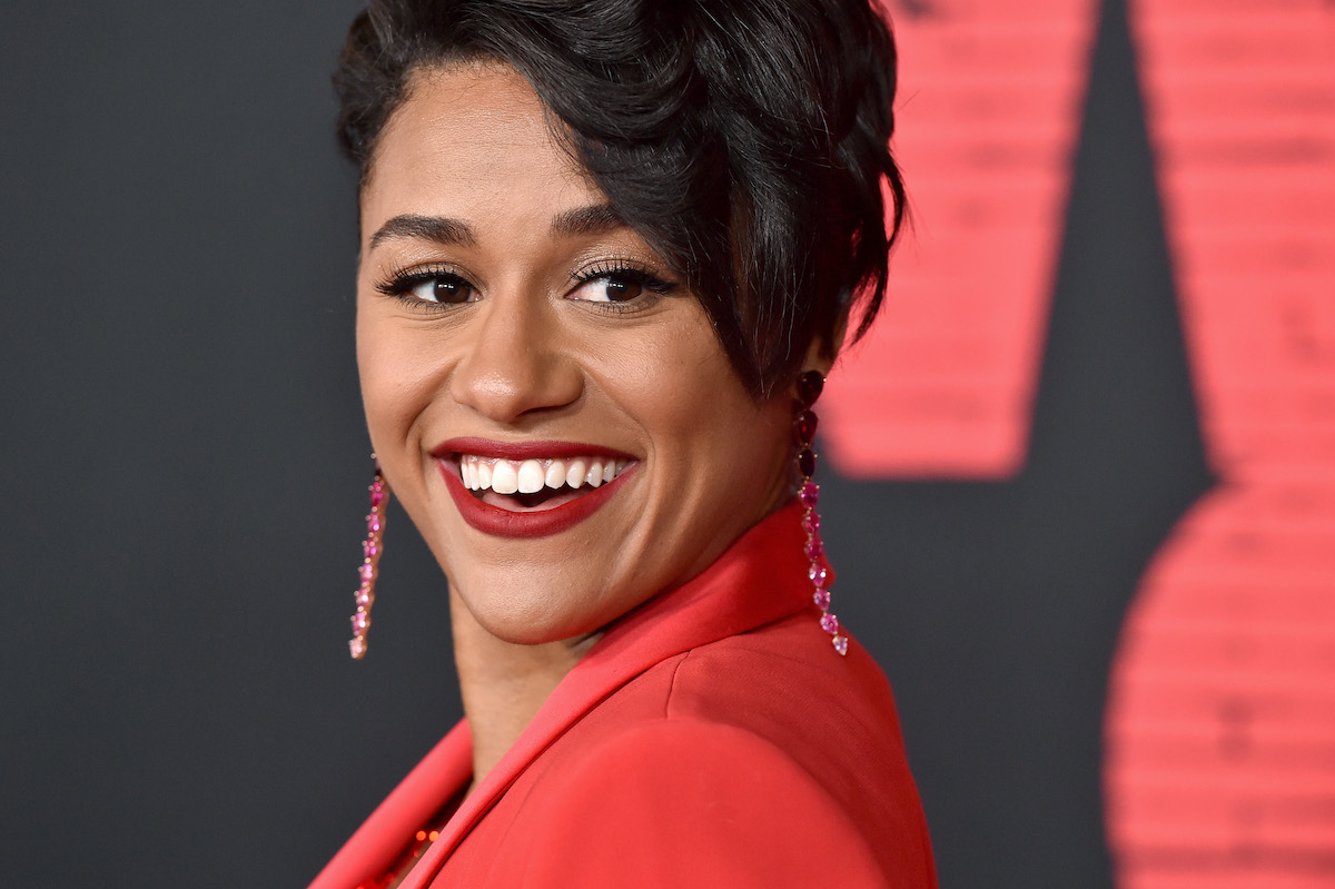 Ariana DeBose smiles in a red jacket and earrings on the red carpet