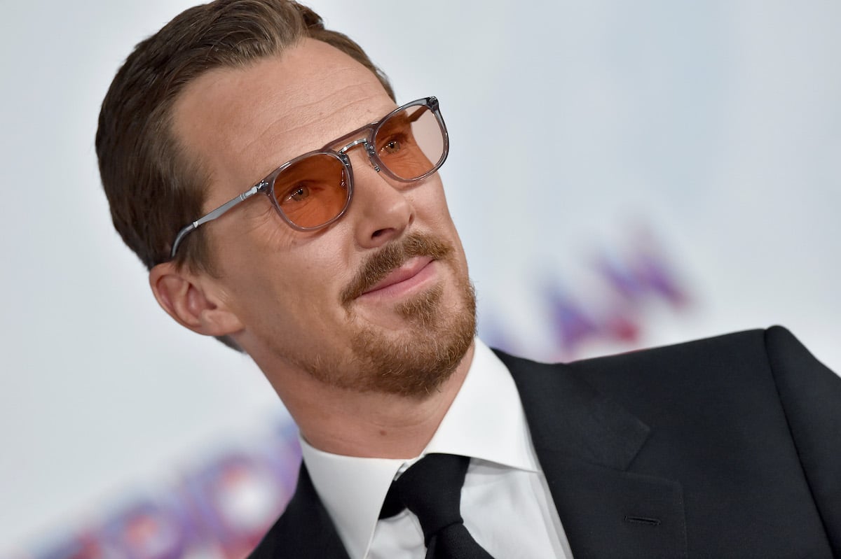 Benedict Cumberbatch wears a dark suit and sunglasses as he smiles on the red carpet