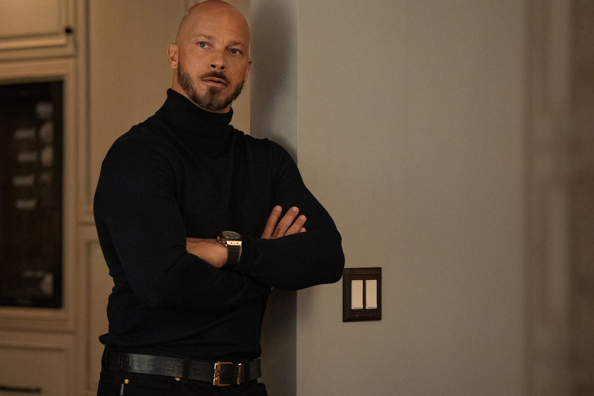 Berto Colon as Lorenzo Tejada wearing all black and leaning against a wall in 'Power Book II: Ghost'