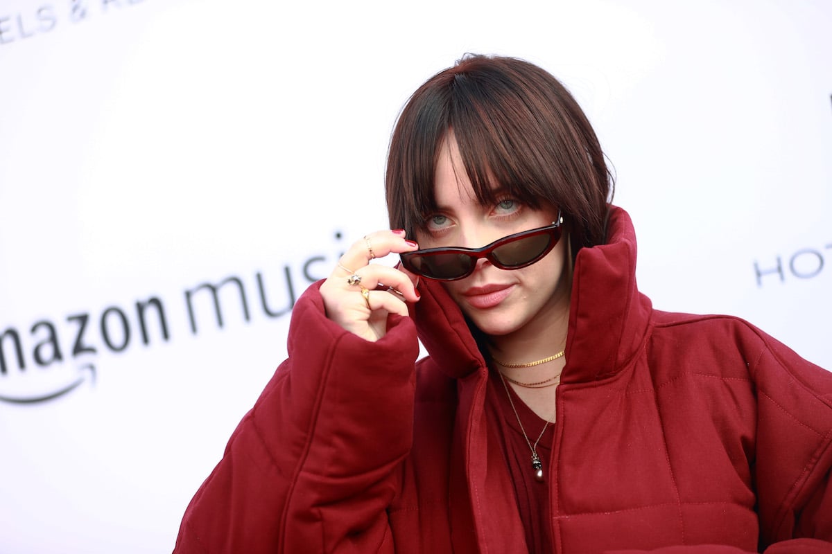 Billie Eilish peers over the top of her sunglasses at an event.