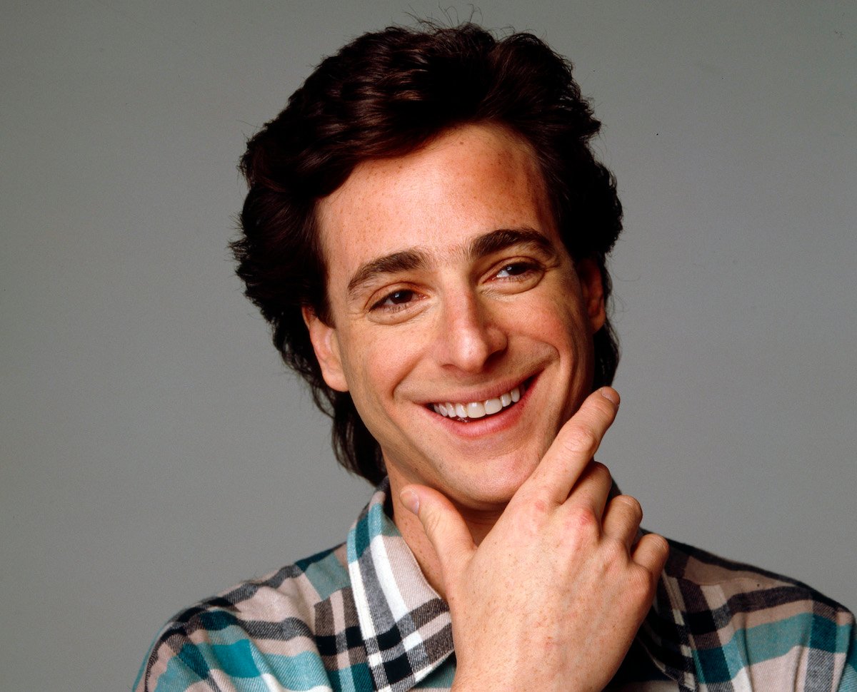 Bob Saget smiles and rubs his chin.