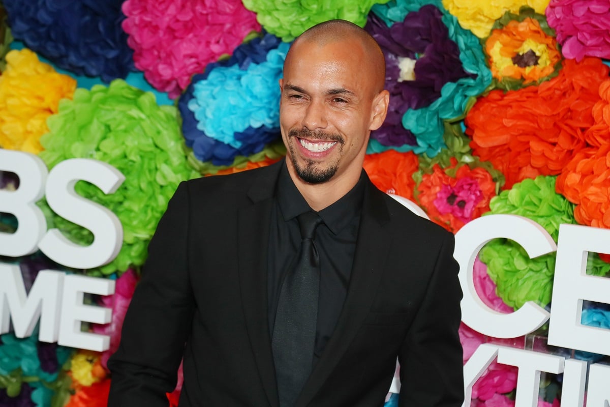 'The Young and the Restless' actor Bryton James wearing a black suit and standing in front of a floral hedge.