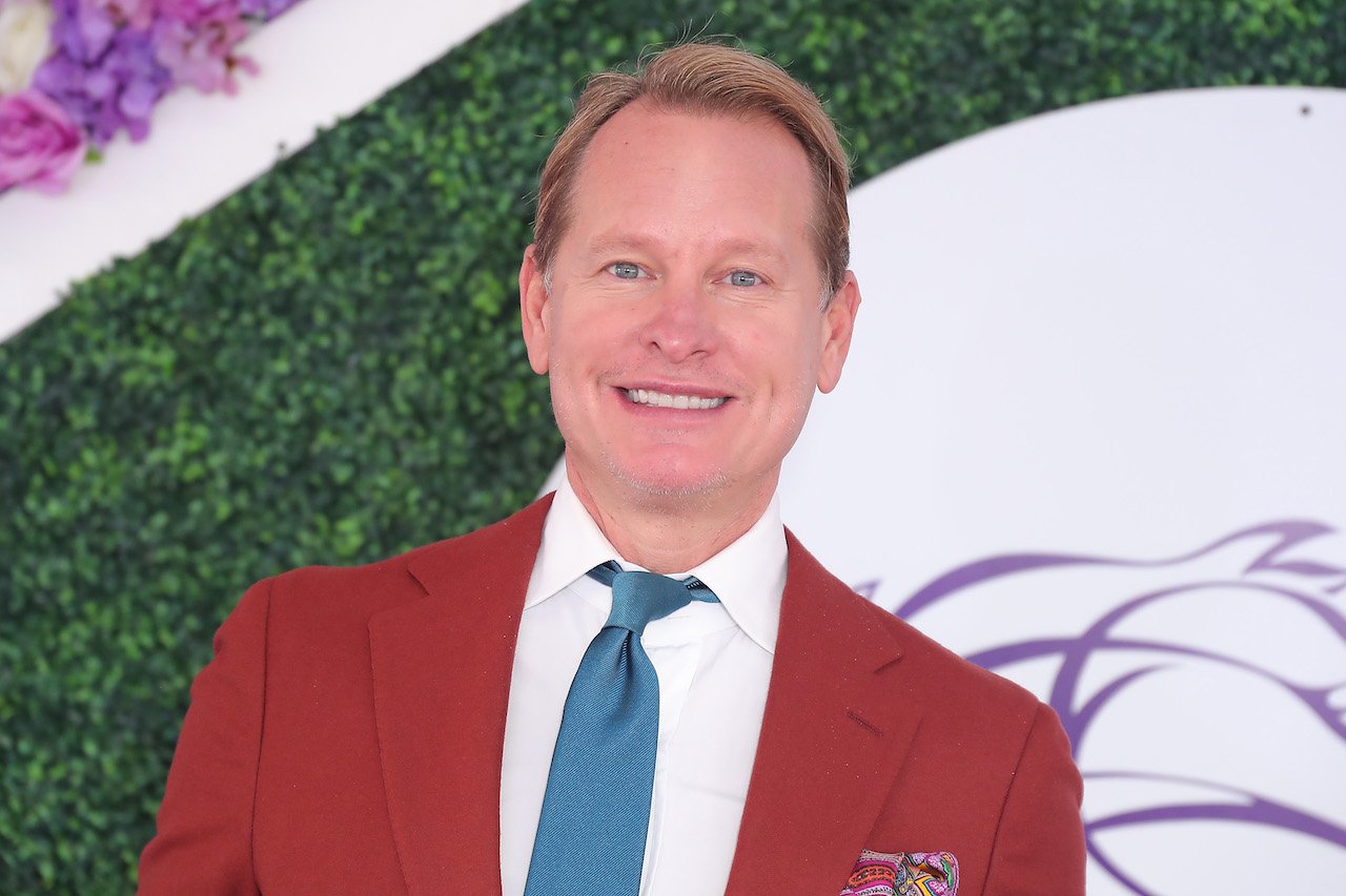 Carson Kressley poses in a red suit and blue tie.