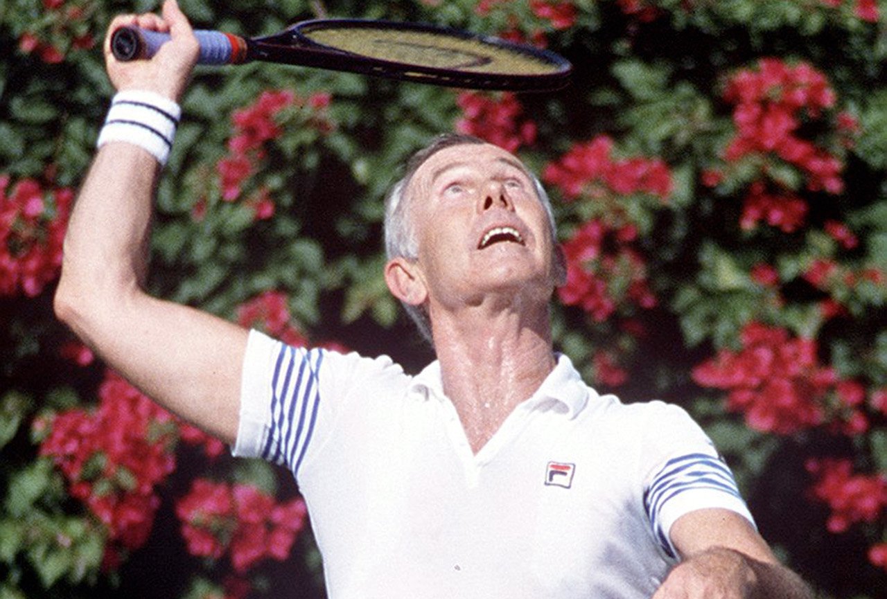 Johnny Carson in white sportswear, jumping to hit a tennis ball c. 1990