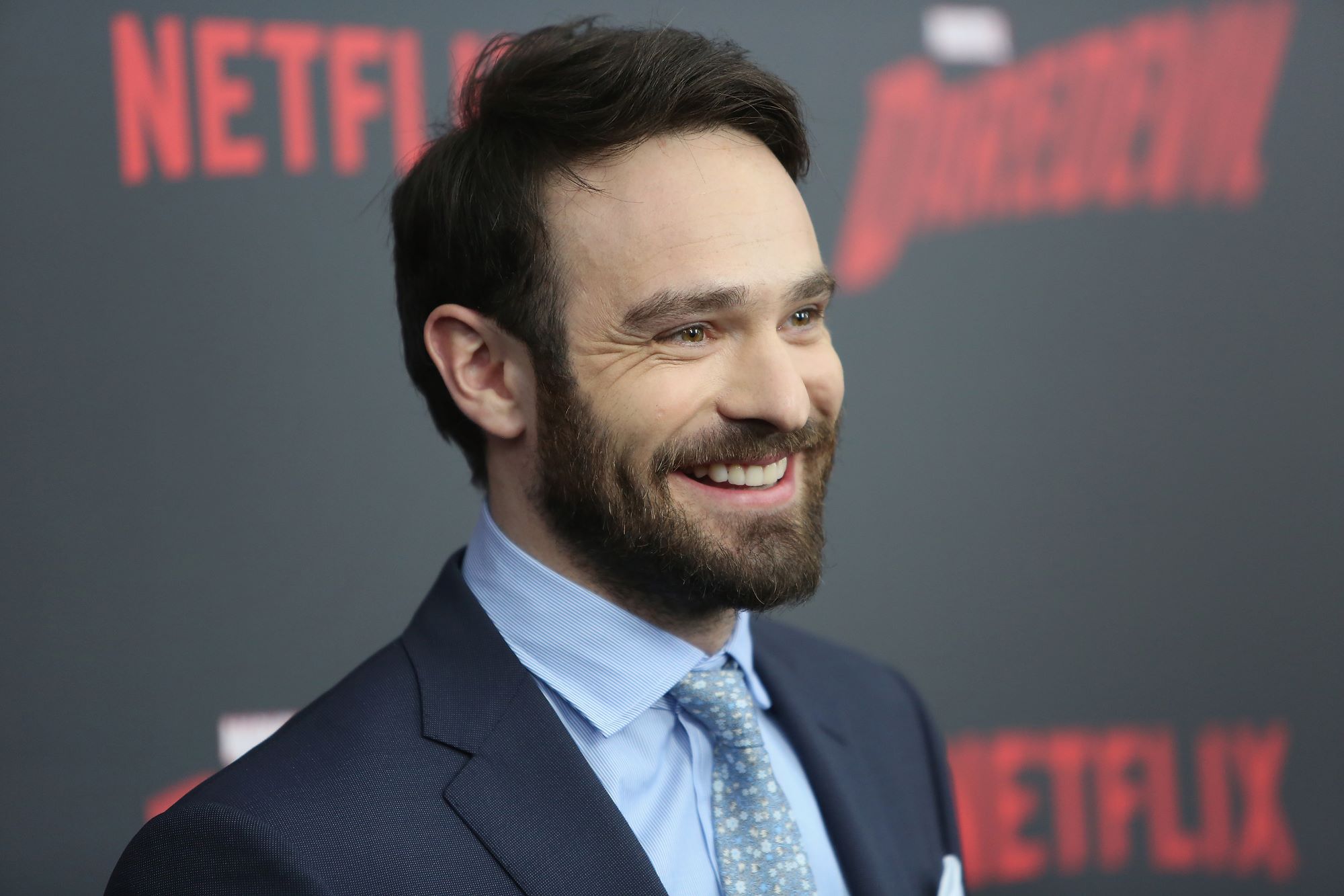 Netflix's 'Daredevil' star Charlie Cox wears a dark blue suit over a light blue button-up shirt and blue patterned tie.