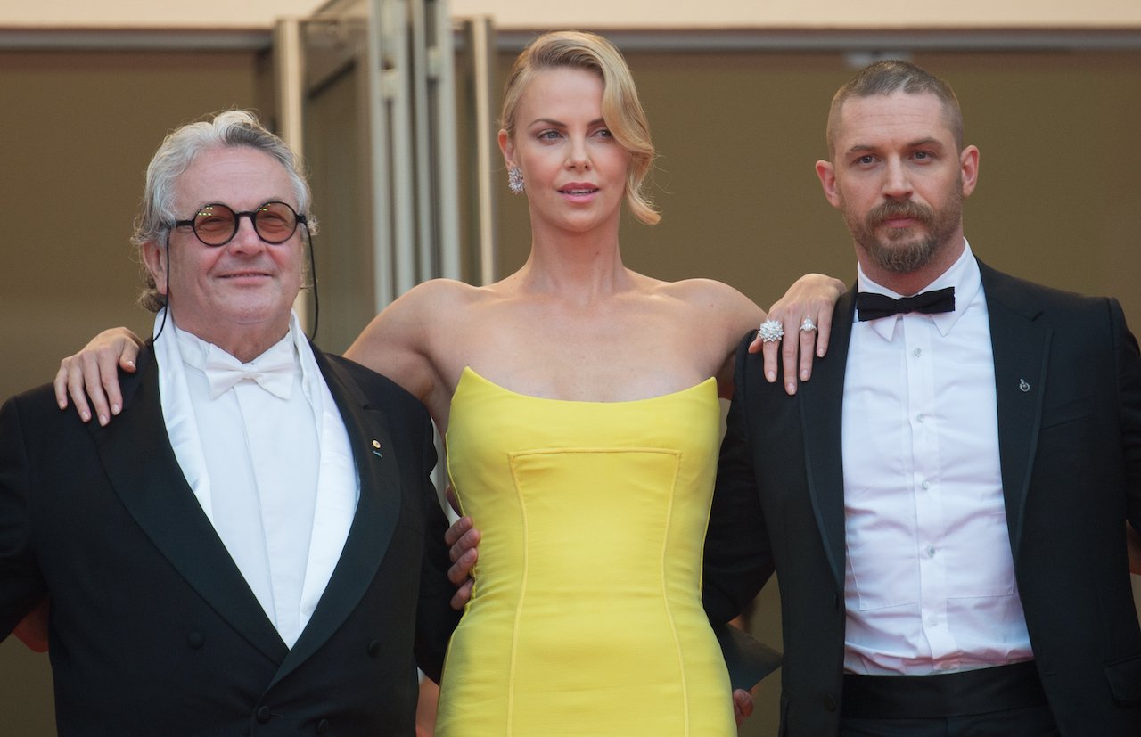 (l-r) George Miller in a black tuxedo, Charlize Theron in a yellow dress, and Tom Hardy in a black tuxedo