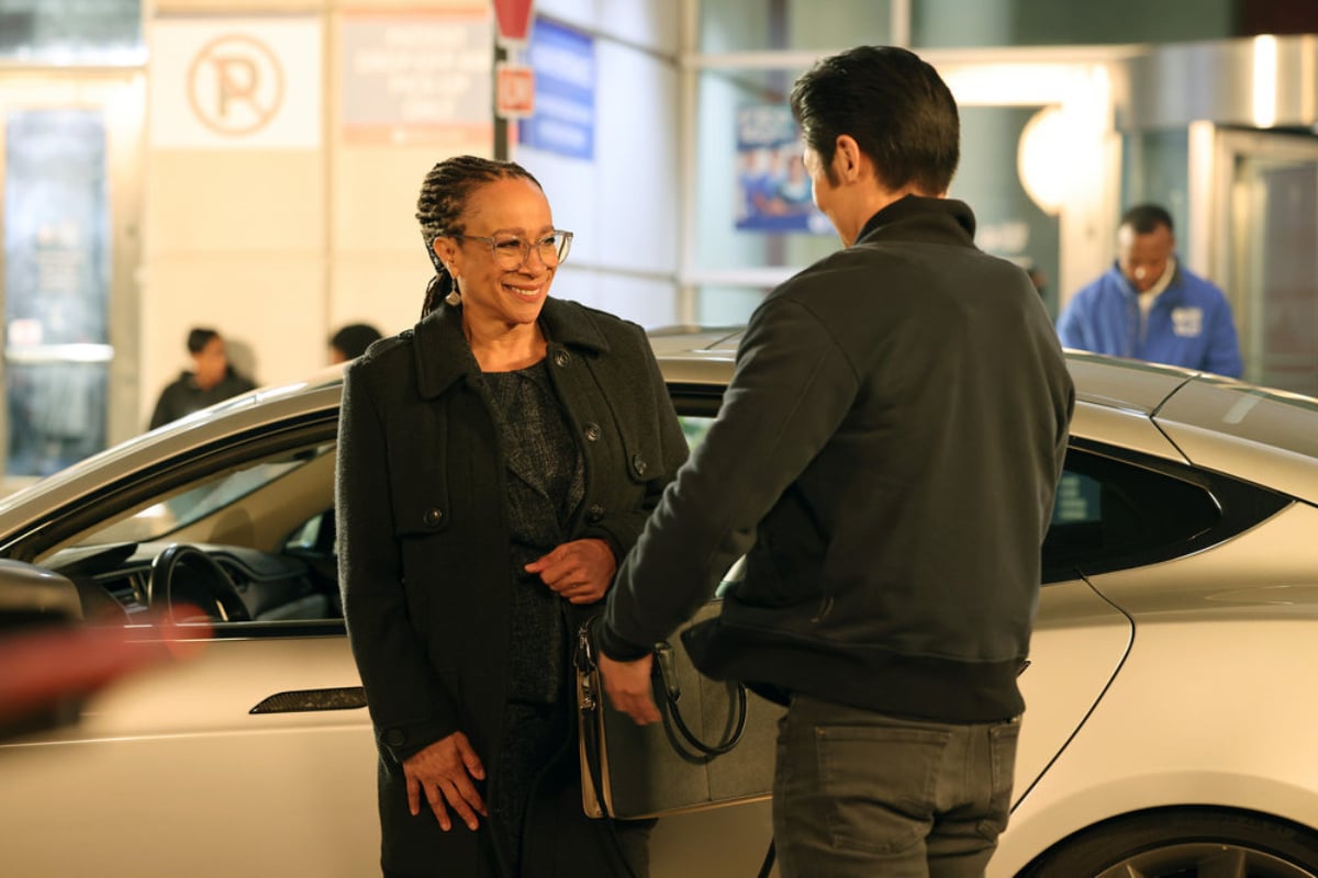 S. Epatha Merkerson as Sharon Goodwin Brian Tee as Ethan Choi in Chicago Med Season 7. Goodwin smiles at Choi. They are standing in front of her car.