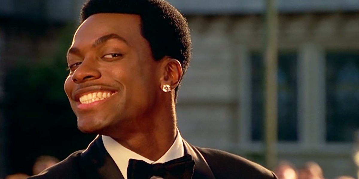 Chris Tucker smiles while wearing a suit and diamond earring in ‘Money Talks’