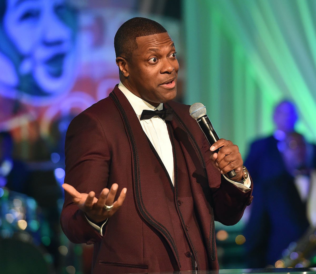 Chris Tucker wears a suit as he speaks onstage