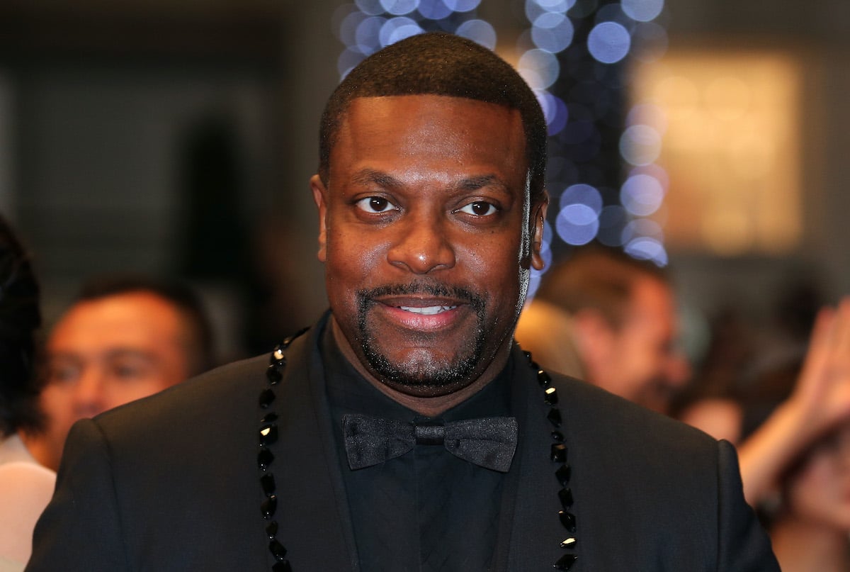 Chris Tucker wears a black suit and smiles