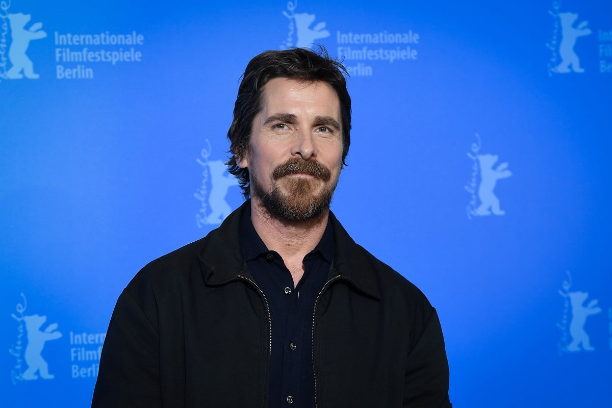 Christian Bale smirking while wearing a black suit.