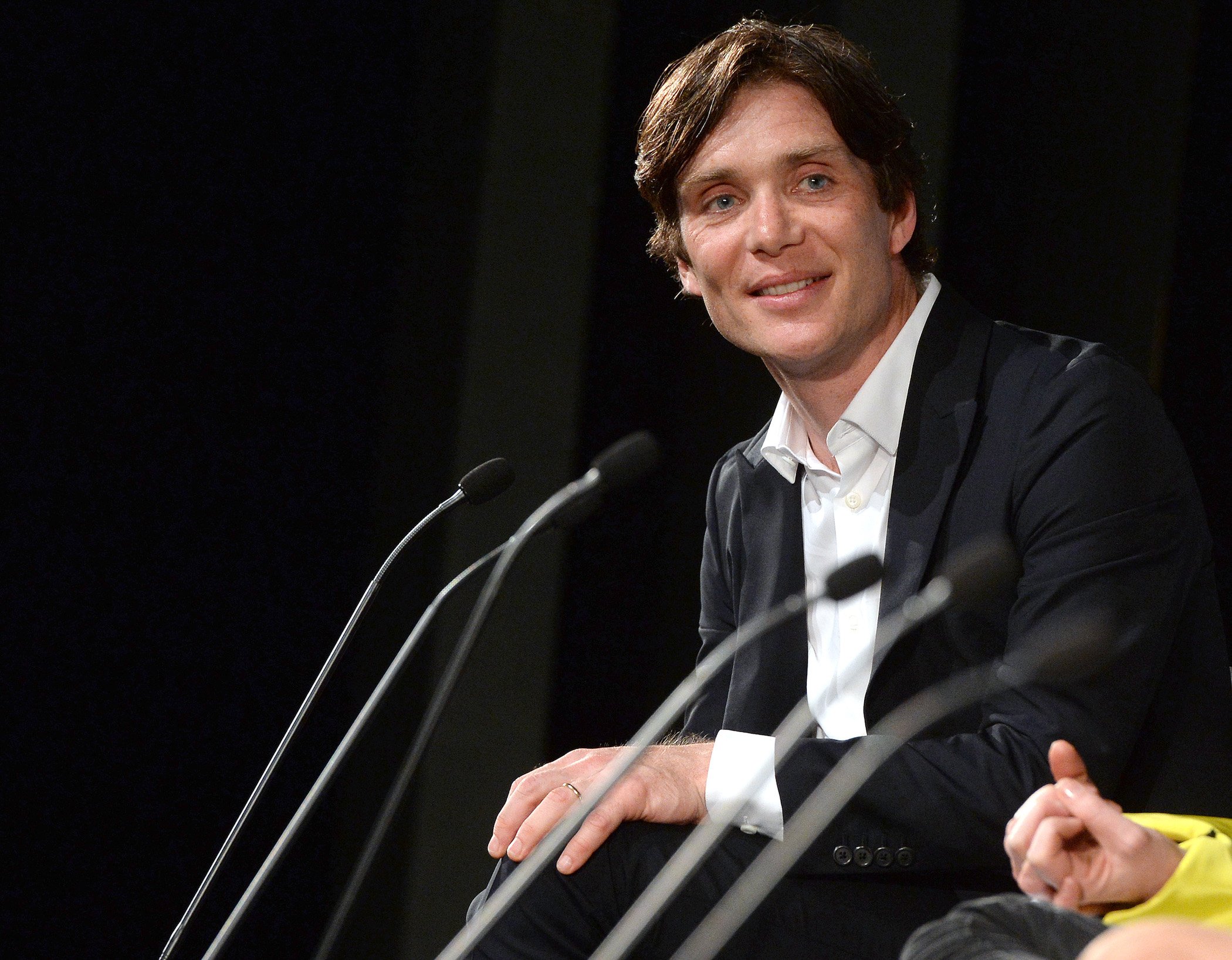 'Peaky Blinders' Season 6 star Cillian Murphy smiling in front of a microphone against a black background