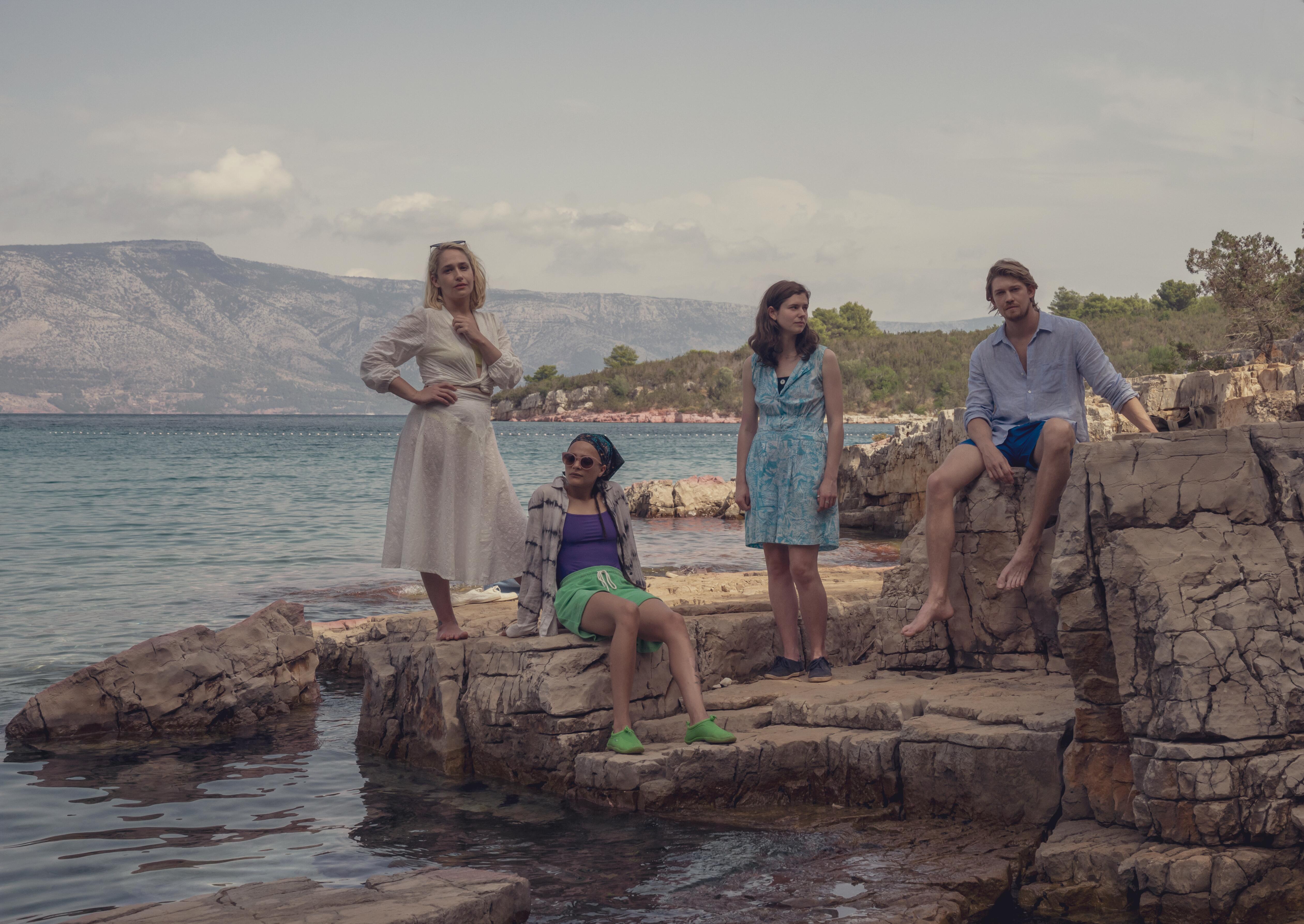 The cast of 'Conversations With Friends' standing on rocks near the waer