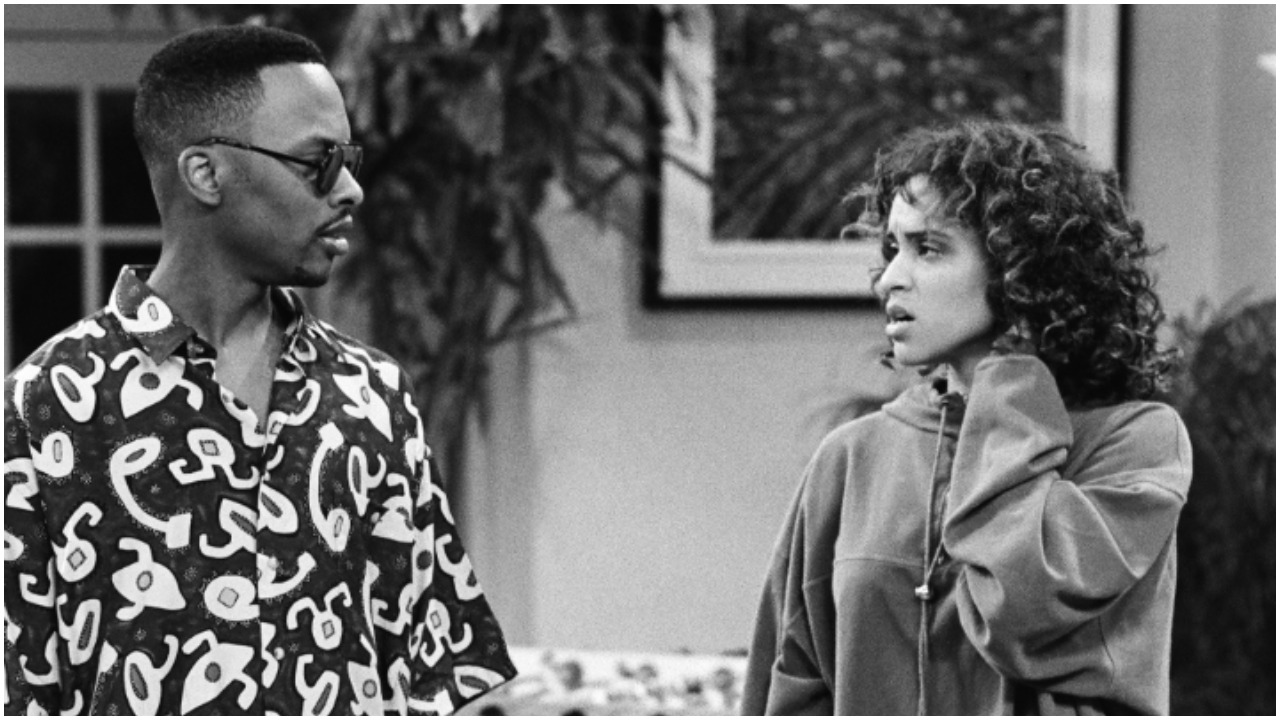 A black and white photo of DJ Jazzy Jeff and Karyn Parsons talking to each other during an episode of 'Fresh Prince of Bel-Air'