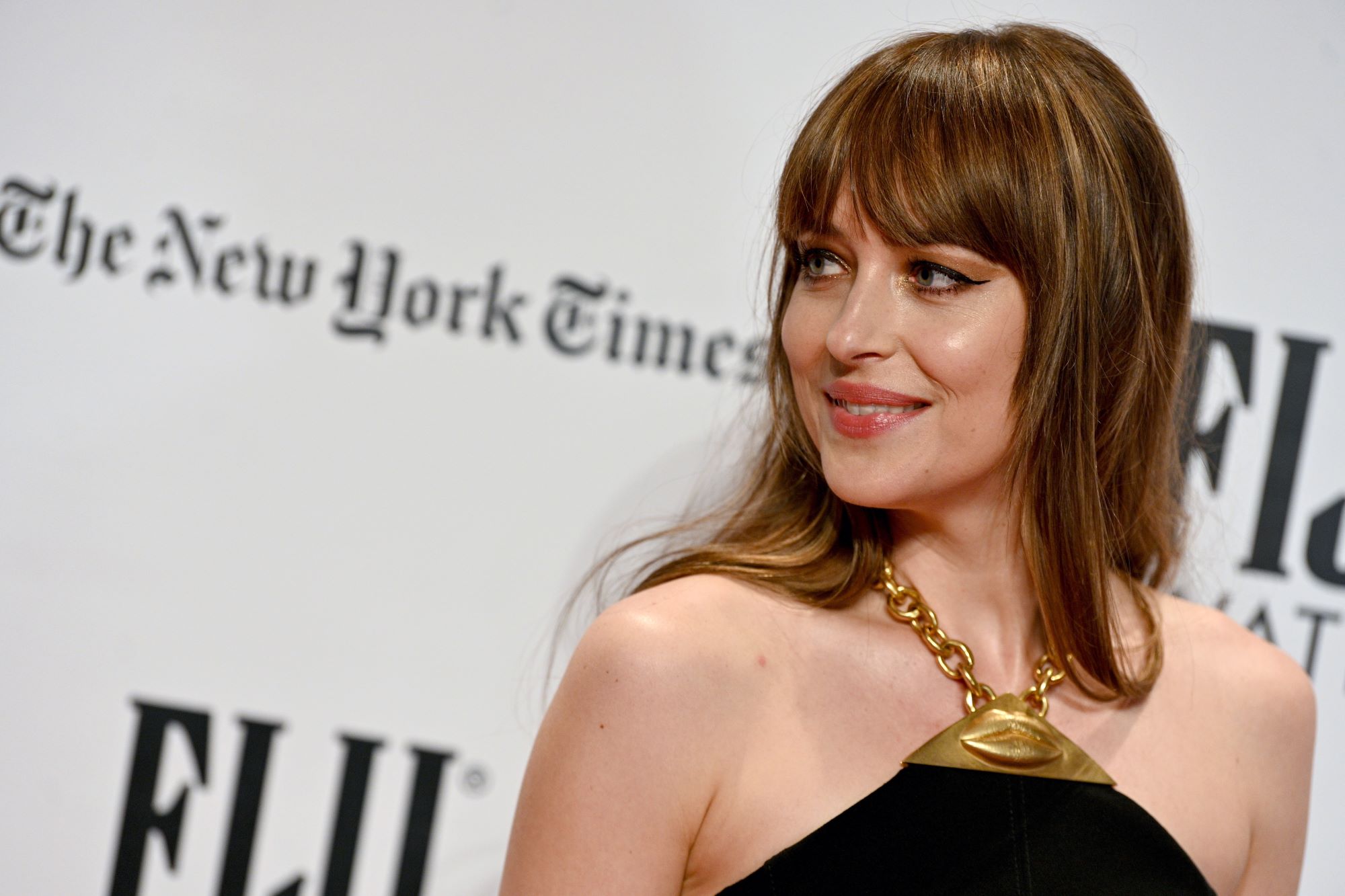 'Madame Web' star Dakota Johnson wears a black dress held up by a gold chain around her neck.