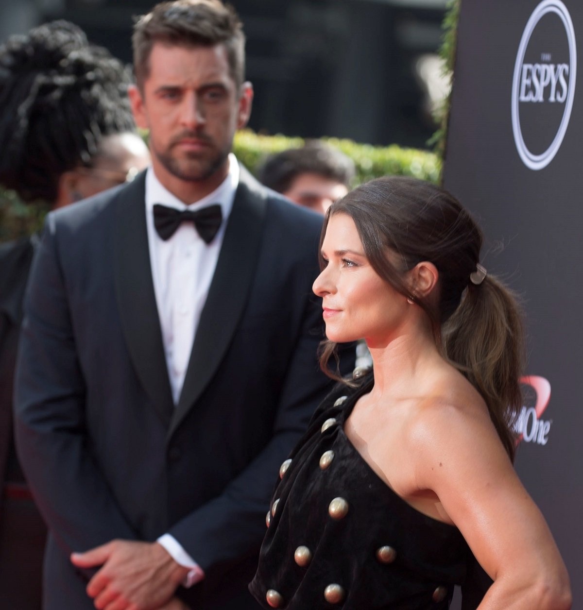 Danica Patrick posing on the ESPYS red carpet while Aaron Rodgers looks on