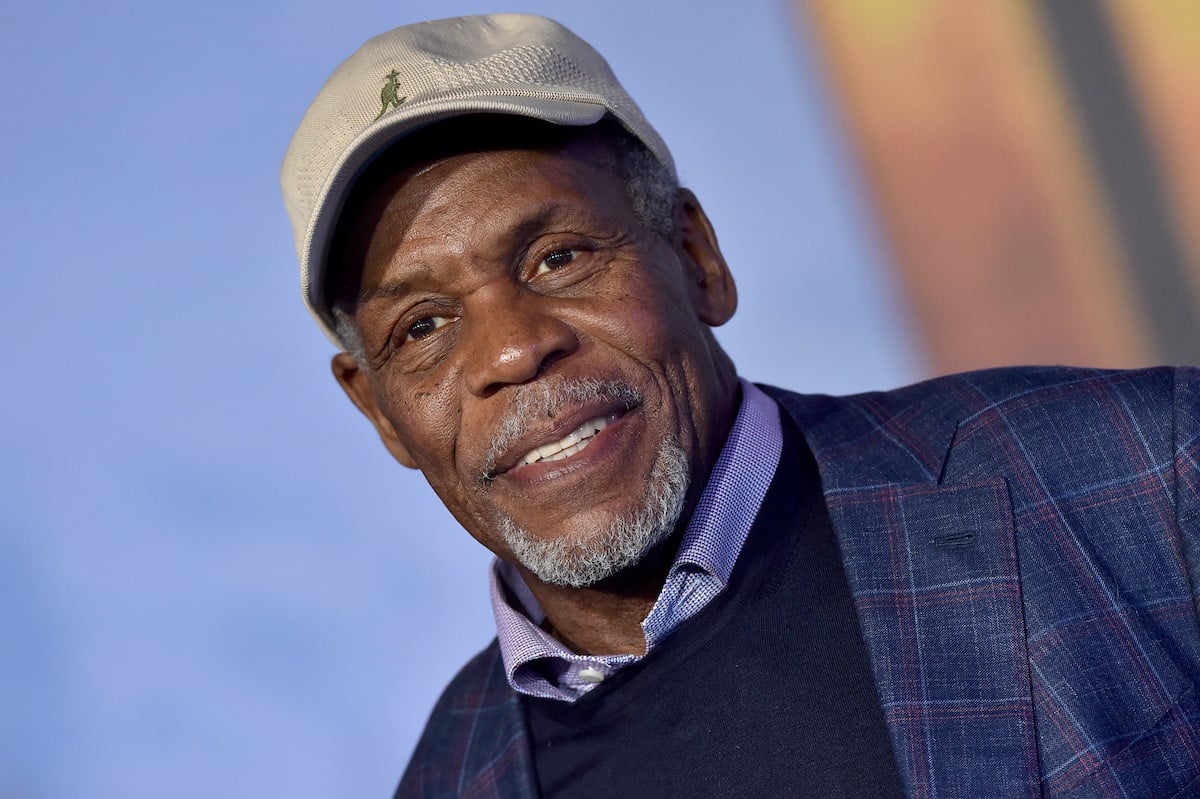Danny Glover smiles while wearing a jacket and cap