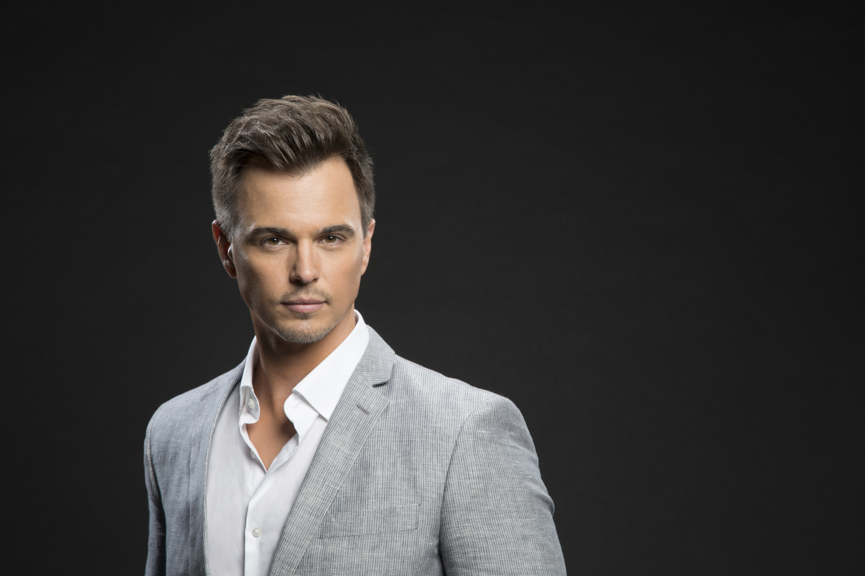 'The Bold and the Beautiful' actor Darin Brooks wearing a grey suit and white shirt standing in front of a black backdrop.