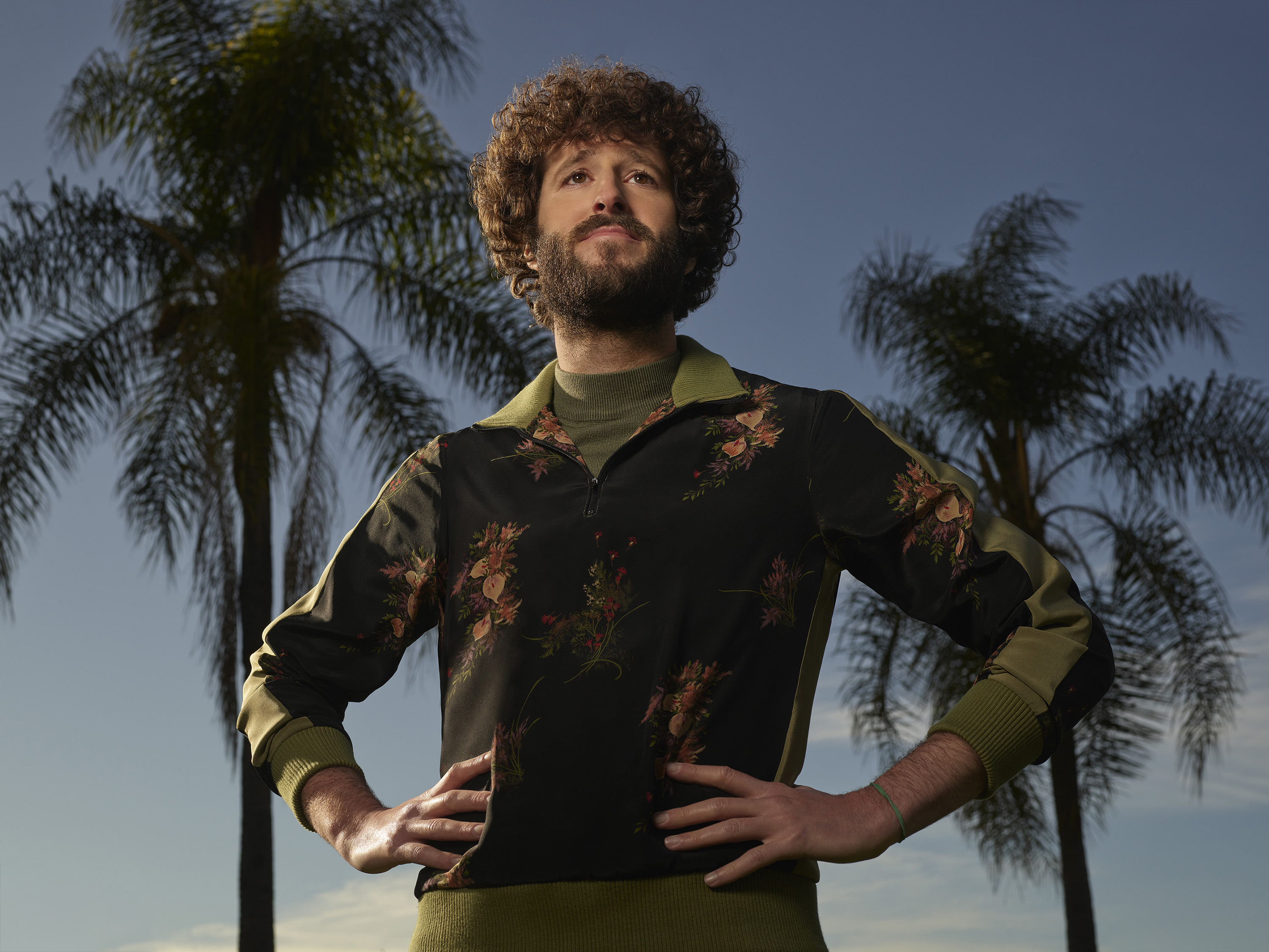 Dave 'Lil Dicky' Burd posing with his hands on his hips in front of palm trees for the FX series 'Dave'. He'll reprise his role in 'Dave' Season 3.