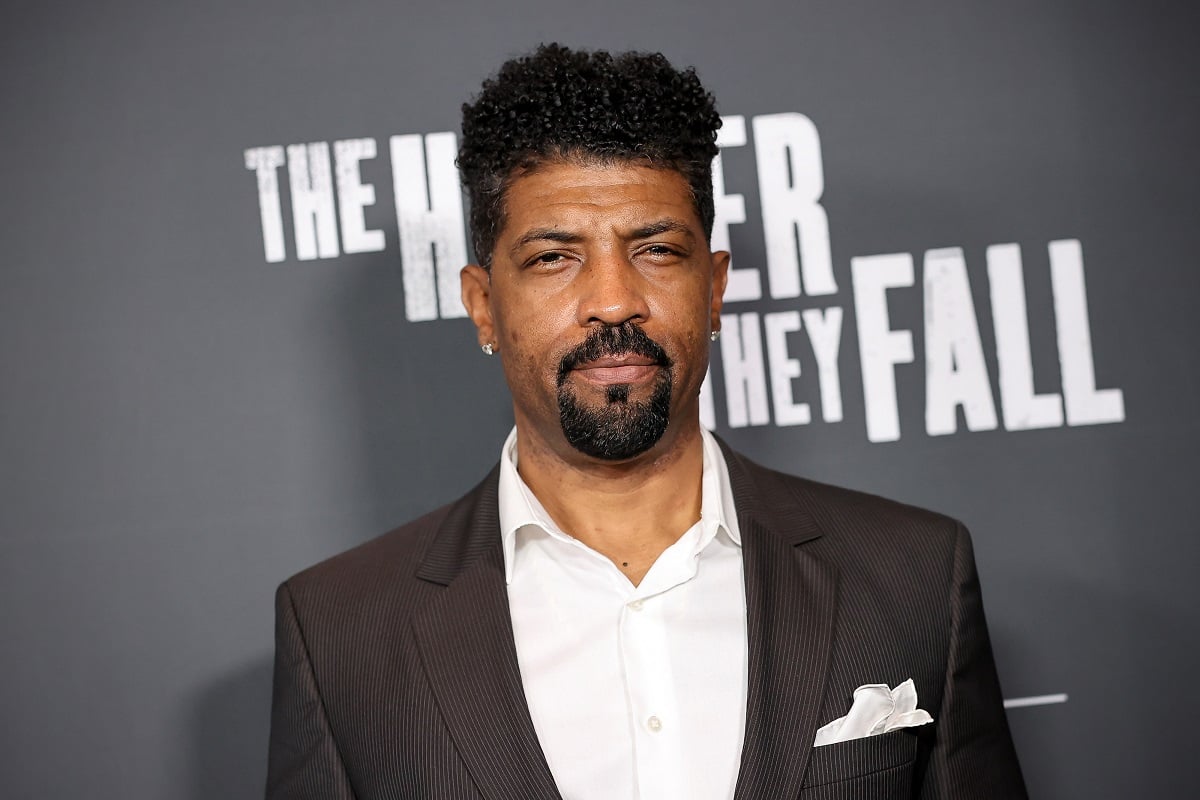 Deon Cole posing while wearing a suit.