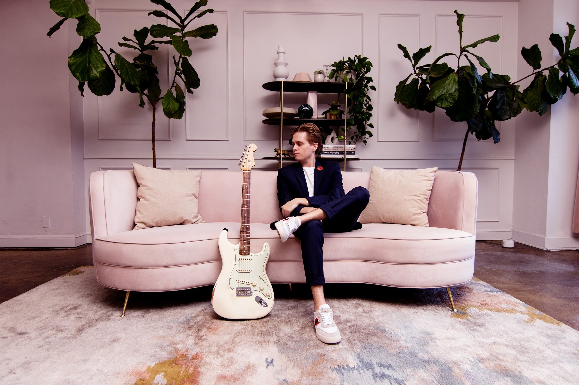 Devin Kennedy sits on a white couch beside an electric guitar