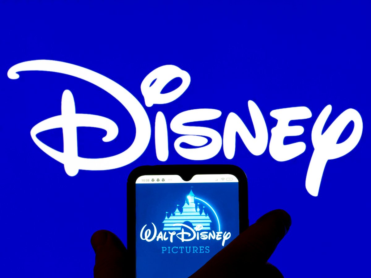 Walt Disney Pictures logo is displayed on a smartphone with the Disney logo in the background