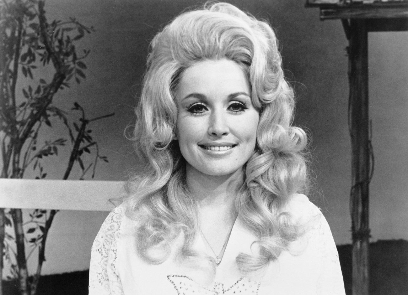 A black-and-white photo of Dolly Parton wearing a bedazzled shirt and sitting in front of a tree