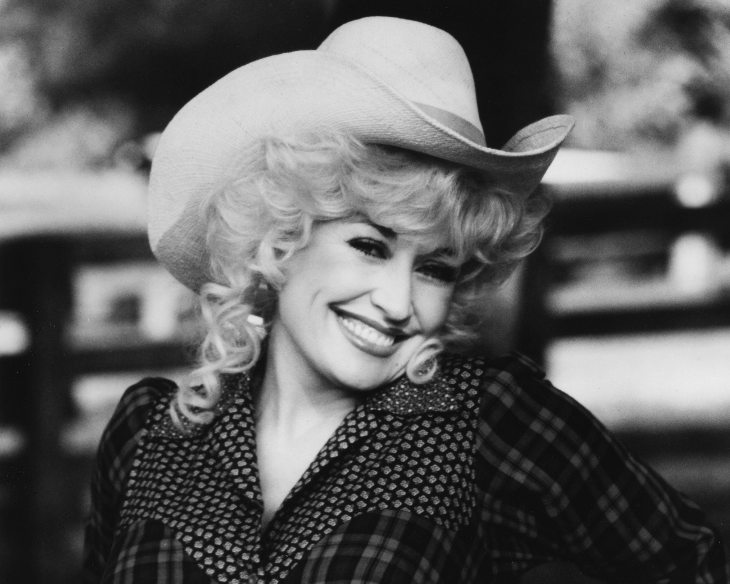 A black and white picture of Dolly Parton wearing a plaid shirt and cowboy hat.