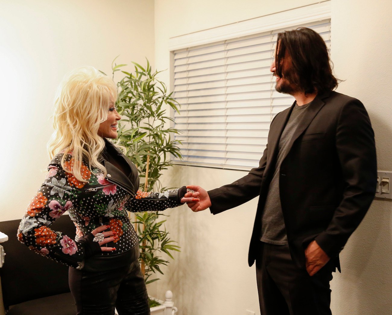 Dolly Parton wearing a multi-colored jacket while holding hands with actor Keanu Reeves on the set of 'The Talk' in 2019.