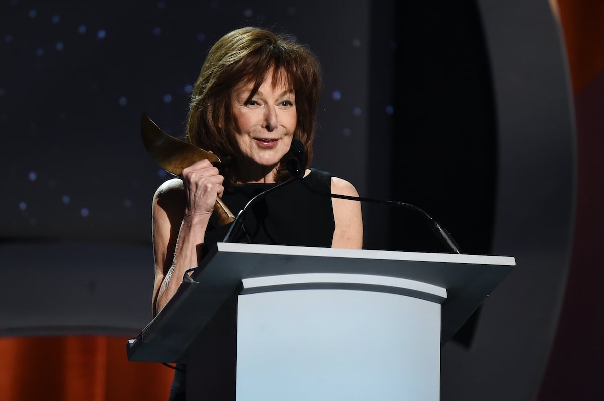 Elaine May holds an award as she stands at a podium