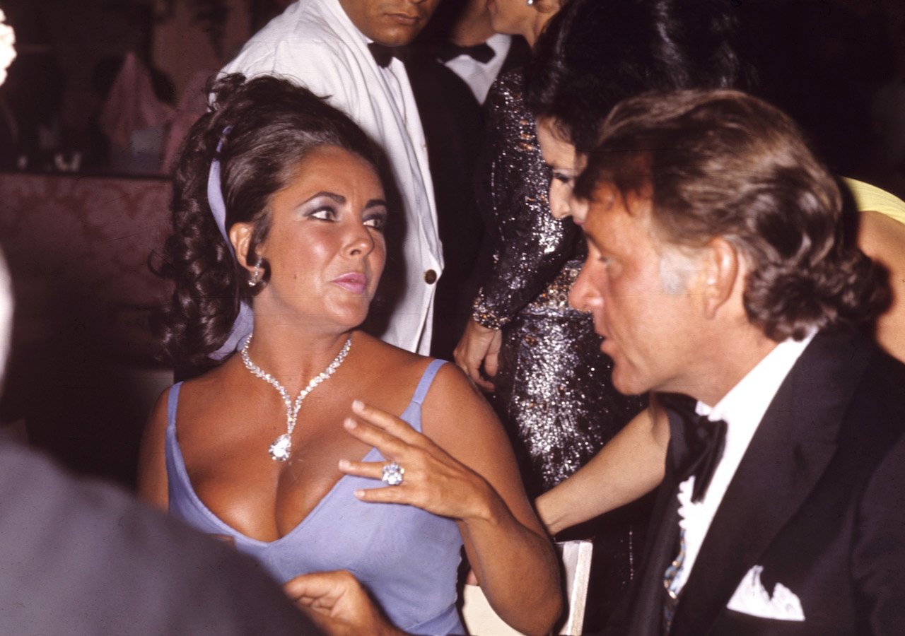 Elizabeth Taylor shows off large diamonds while seated at a table next to Richard Burton