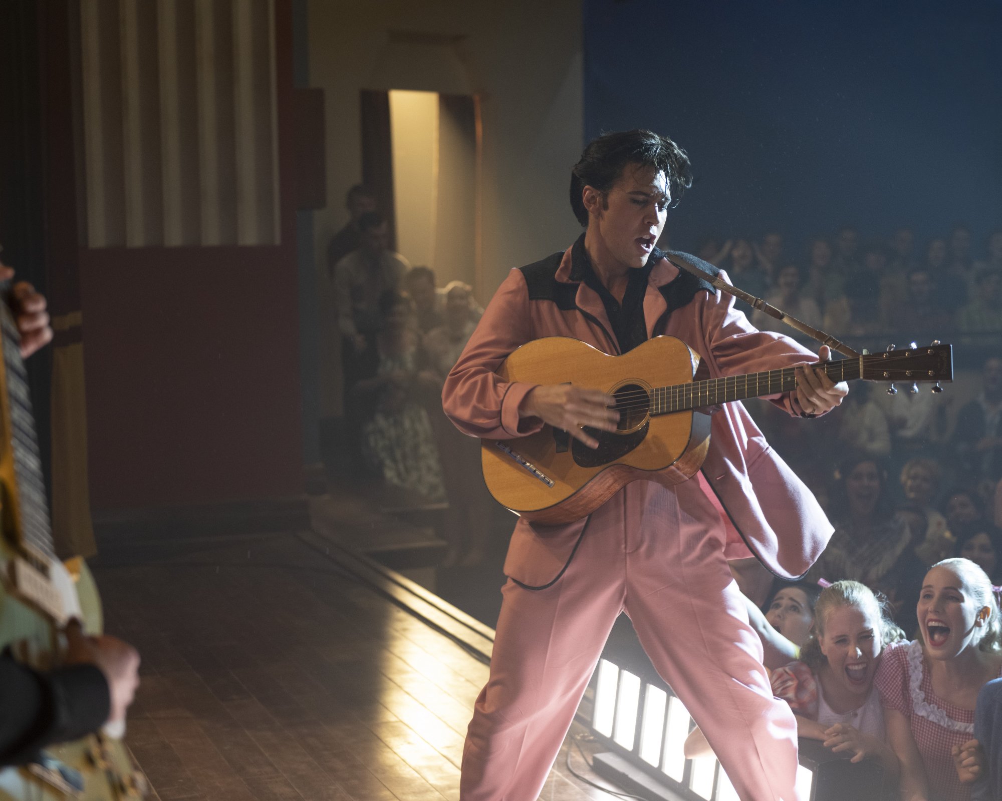 'Elvis' trailer Austin Butler as Elvis Presley wearing pink and playing the guitar on stage
