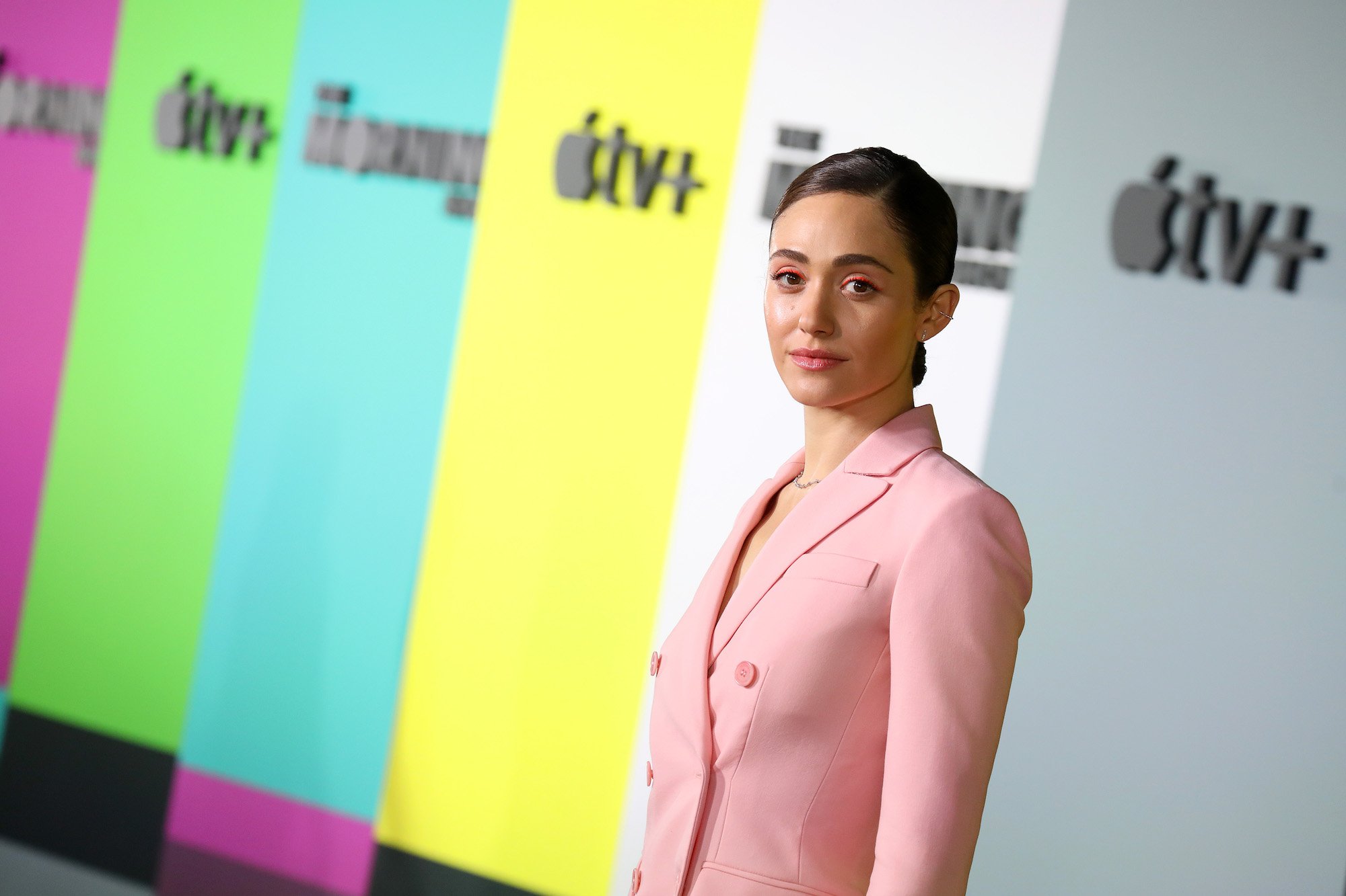 Emmy Rossum looks into camera wearing a pink blazer on an Apple TV+ red carpet