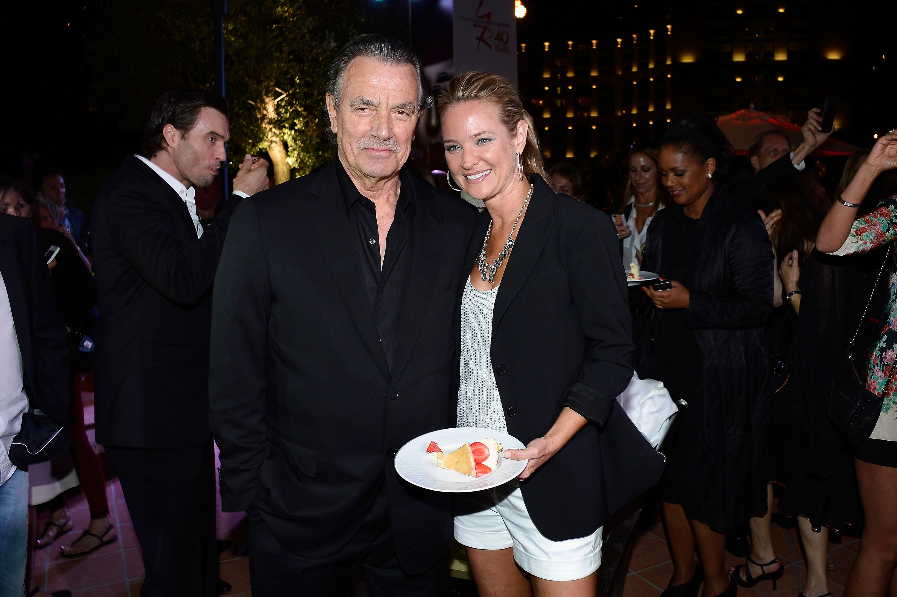 'The Young and the Restless' actor Eric Braeden in a black suit, and Sharon Case in a white outfit with black blazer.