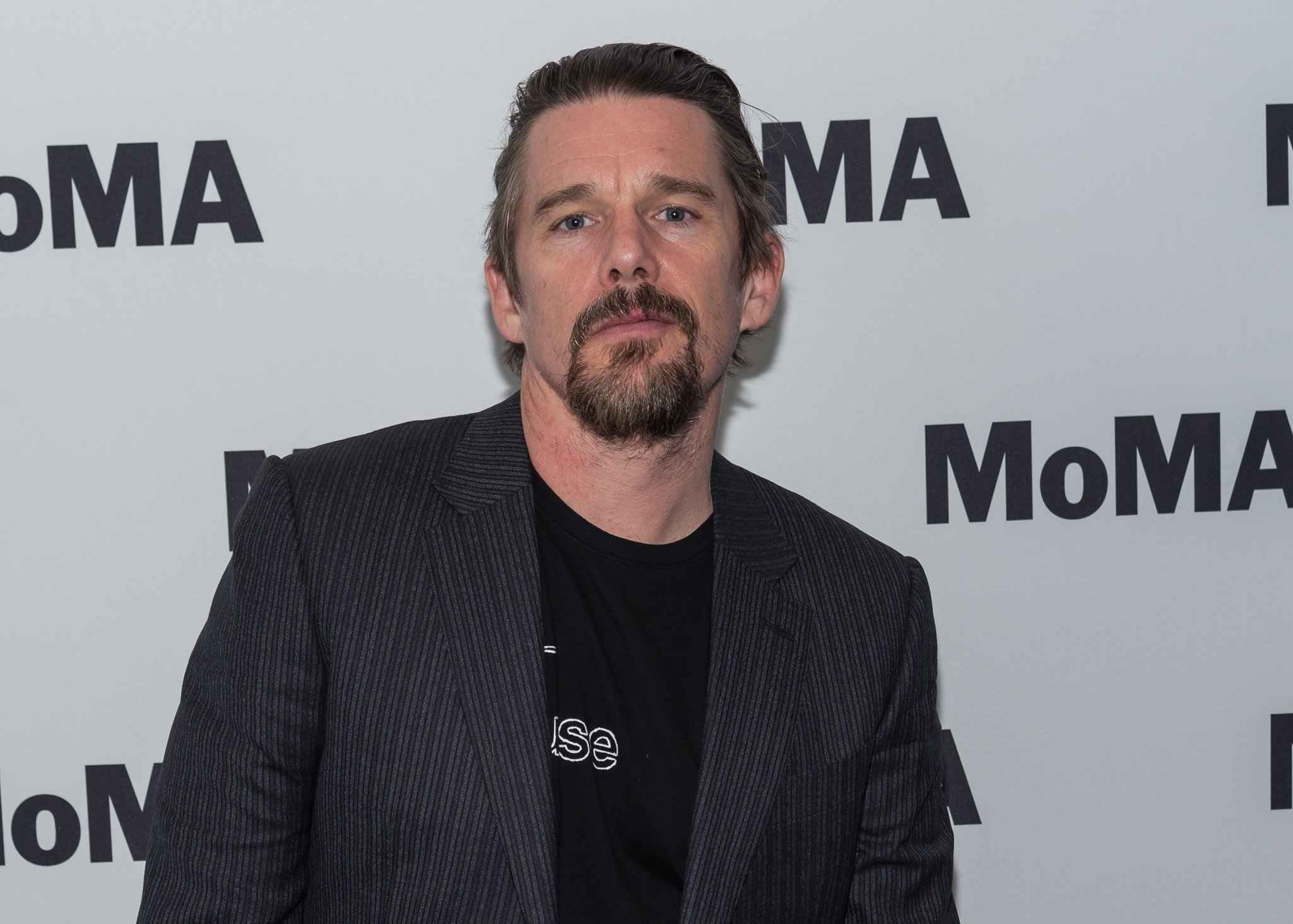 'Moon Knight' actor Ethan Hawke wears a dark gray striped suit jacket over a black shirt.