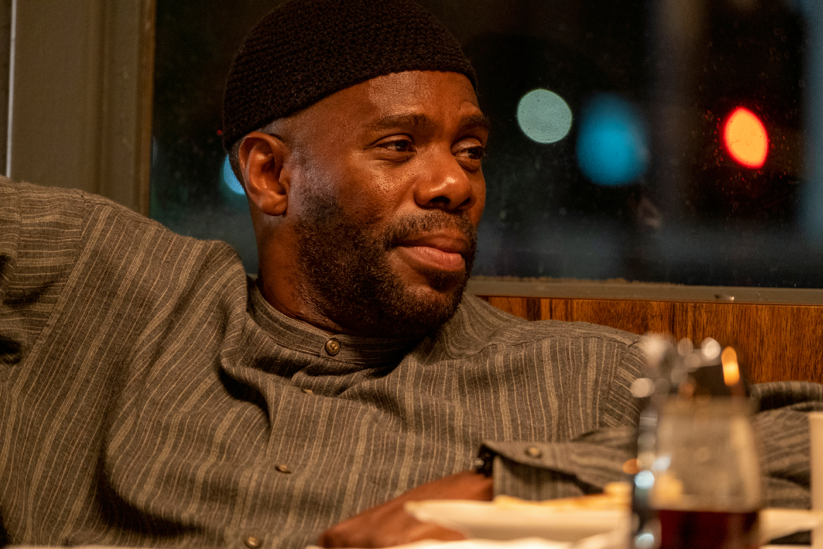 Colman Domingo as Ali in Euphoria Season 2. Ali sits at a diner booth wearing a grey striped shirt and a black cap.