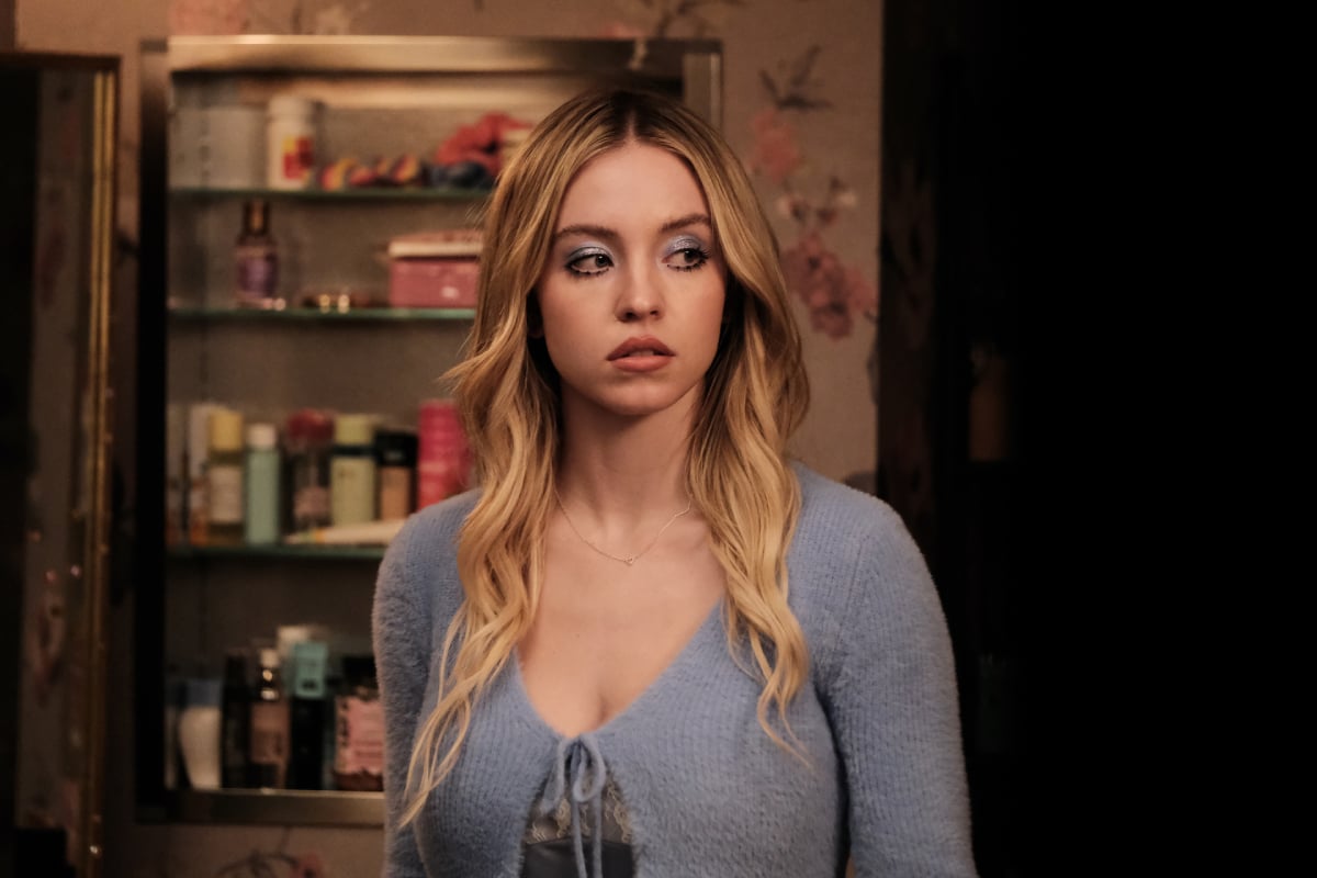 Sydney Sweeney as Cassie in Euphoria Season 2. Cassie has curled blonde hair. She wears a blue top and blue eyeshadow.