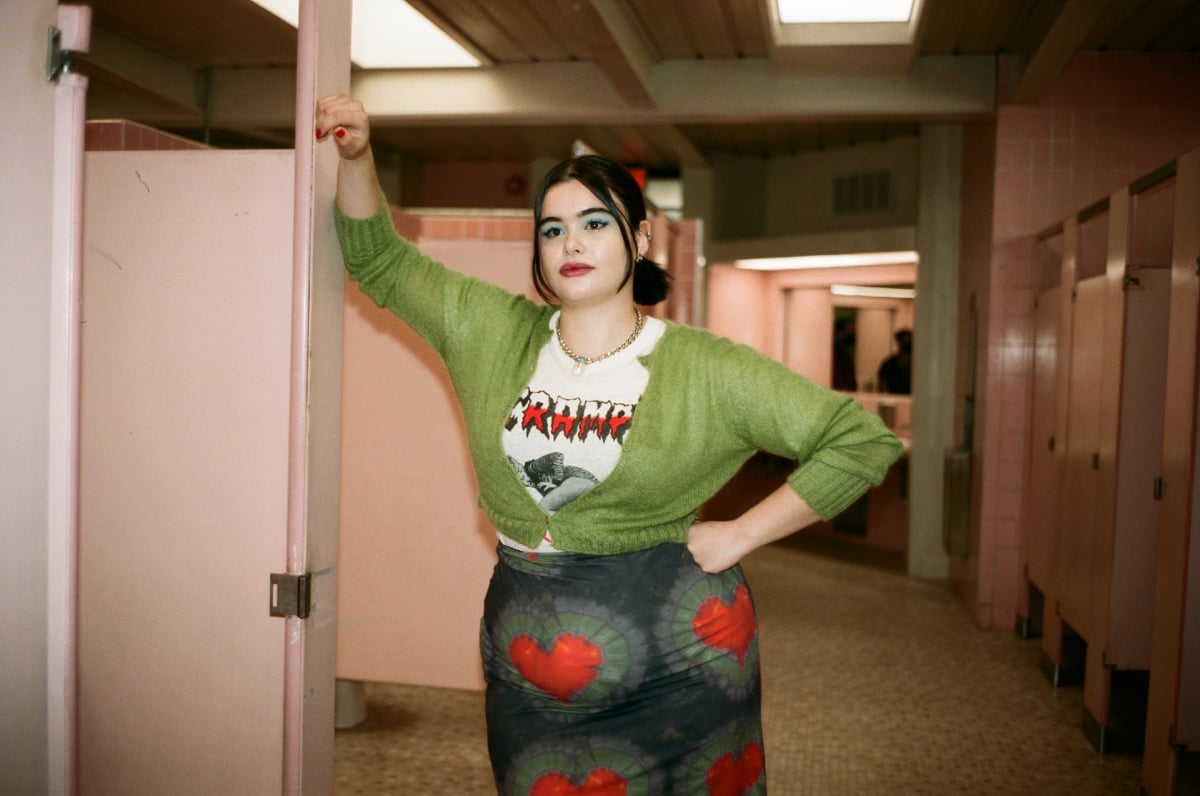Barbie Ferreira as Kat Hernandez in Euphoria Season 2. Kat wears a skirt with hearts on it, graphic tee, and green cardigan.