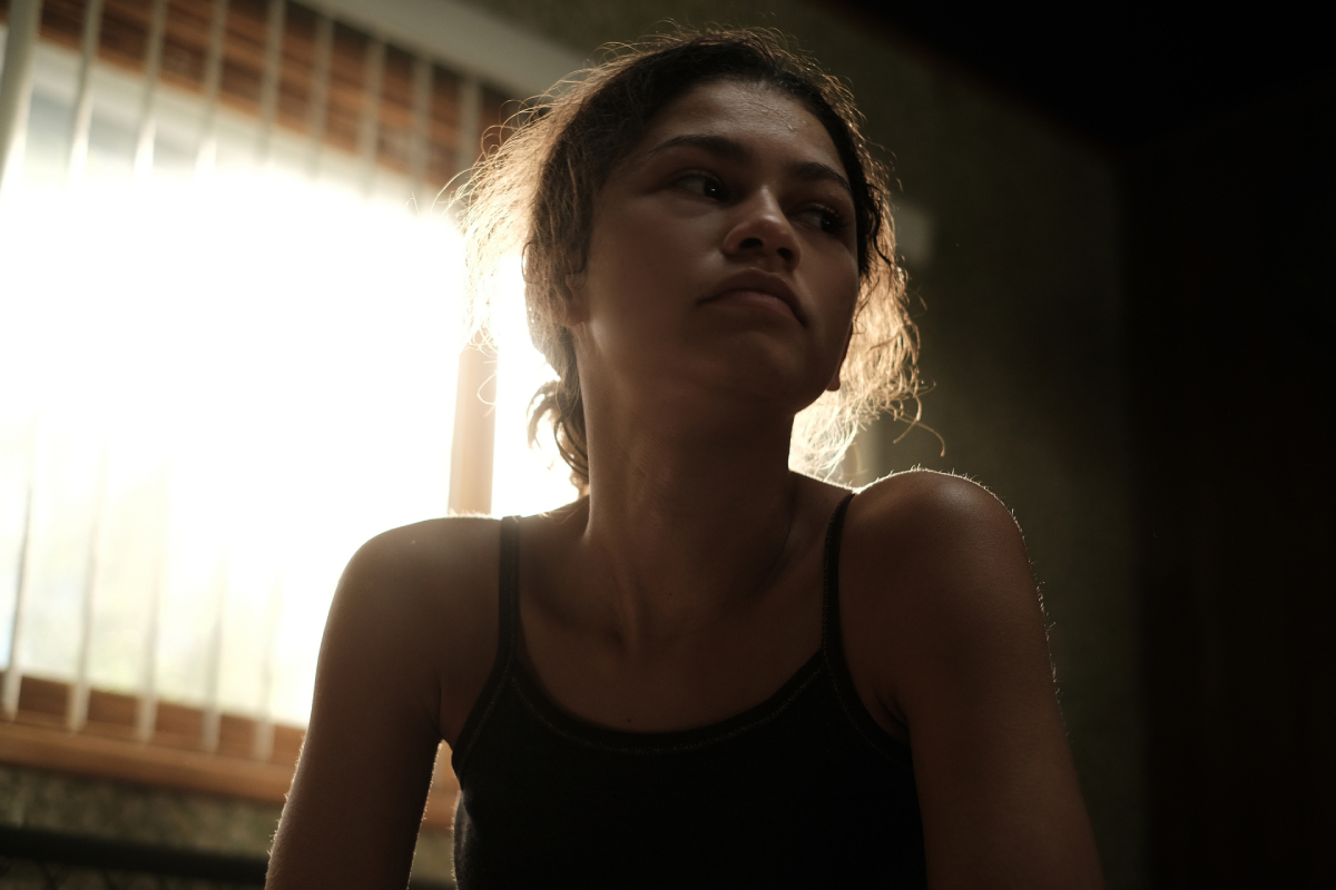Zendaya as Rue Bennett in 'Euphoria' Season 2. Rue sits in front of a window wearing a black tank top.