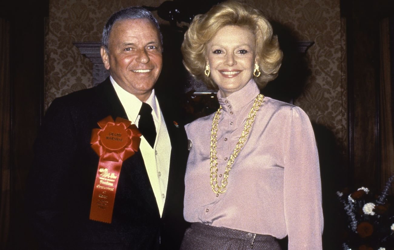 Frank Sinatra wears a suit and a red Grand Marshal ribbon. Barbara Sinatra wears a purple shirt and gold jewelry.