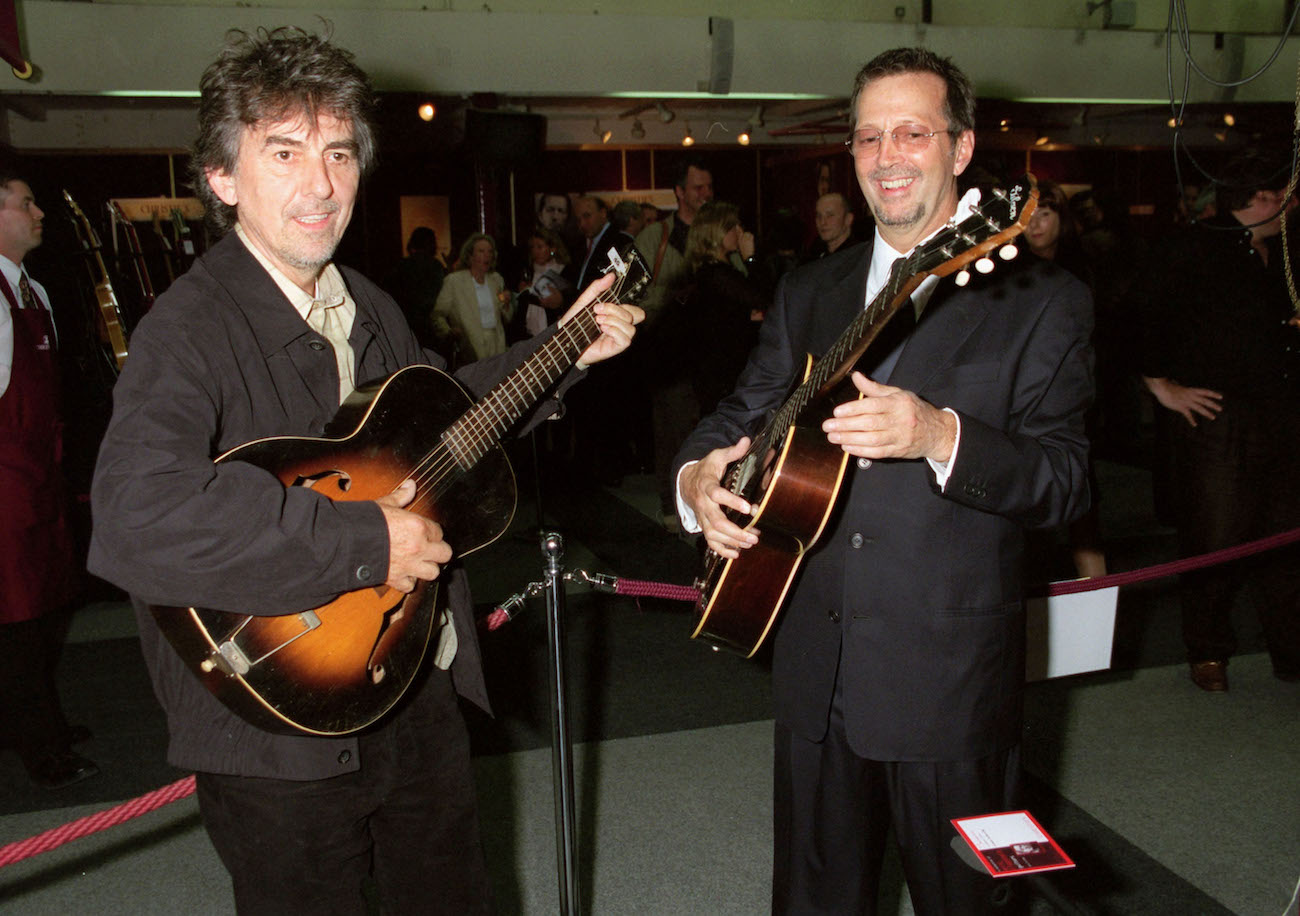 George Harrison and Eric Clapton wearing suits and looking at guitars on offer at Christie's Auction in 1999.