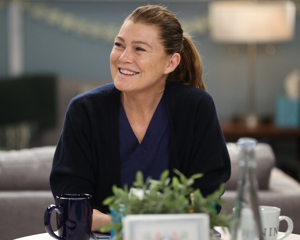 Ellen Pompeo as Meredith Grey smiles wearing blue scrubs on 'Grey's Anatomy'.