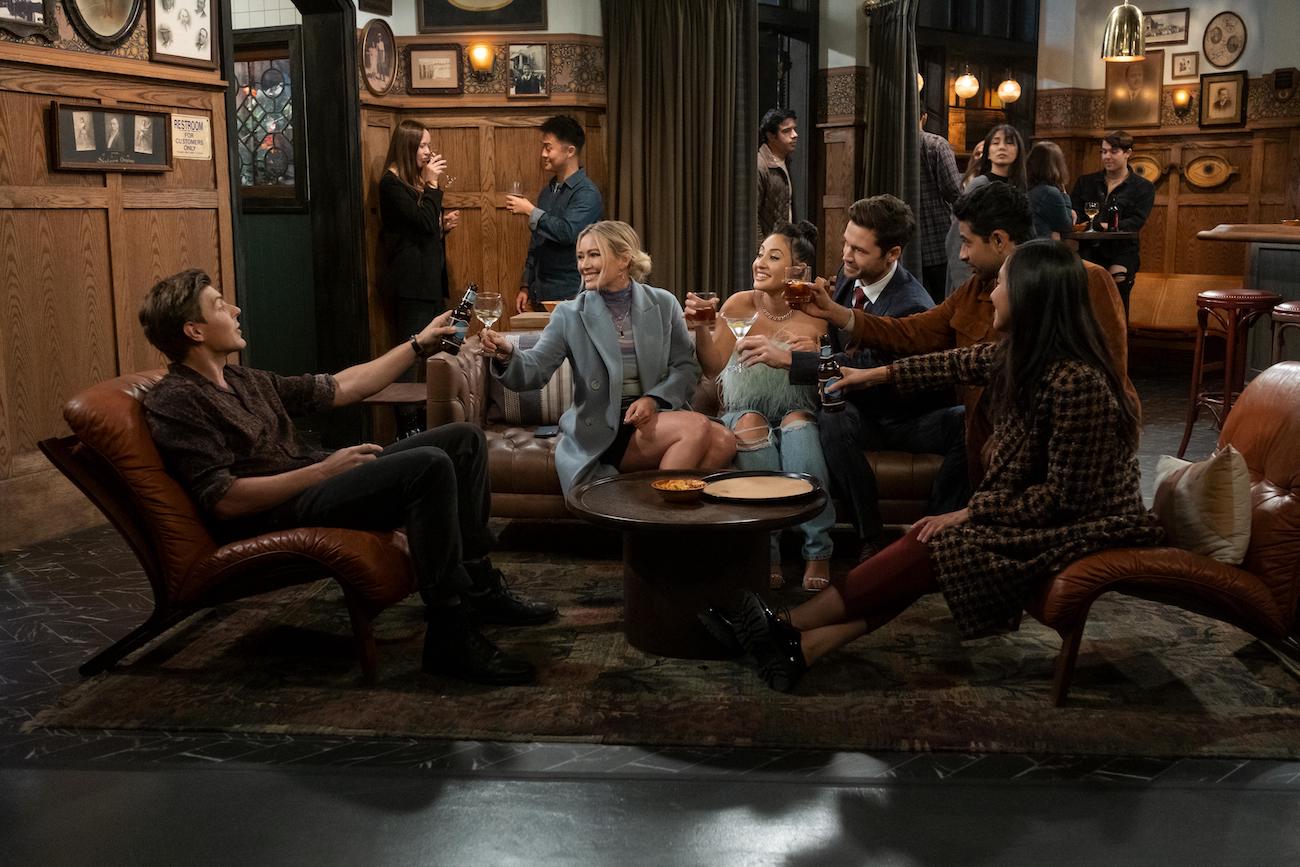 Jesse (Chris Lowell), Sophie (Hilary Duff), Valentina (Francia Raisa), Charlie (Tom Ainsley), Sid (Suraj Sharma), and Ellen (Tien Tran) toast at the bar in the 'FOMO' episode of 'How I Met Your Father' Season 1