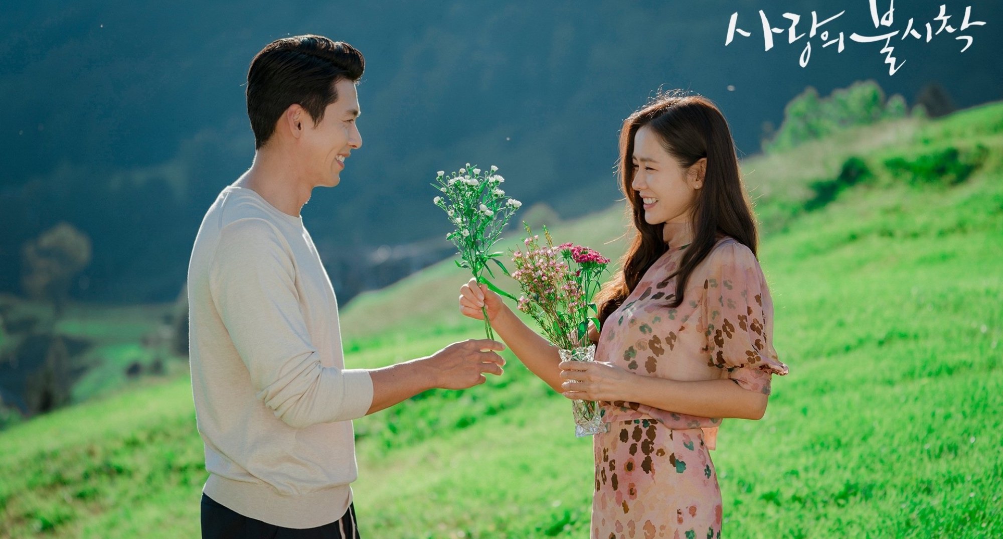 Hyun Bin and Son Ye-jin in 'Crash Landing On You' K-drama facing each other in a meadow.