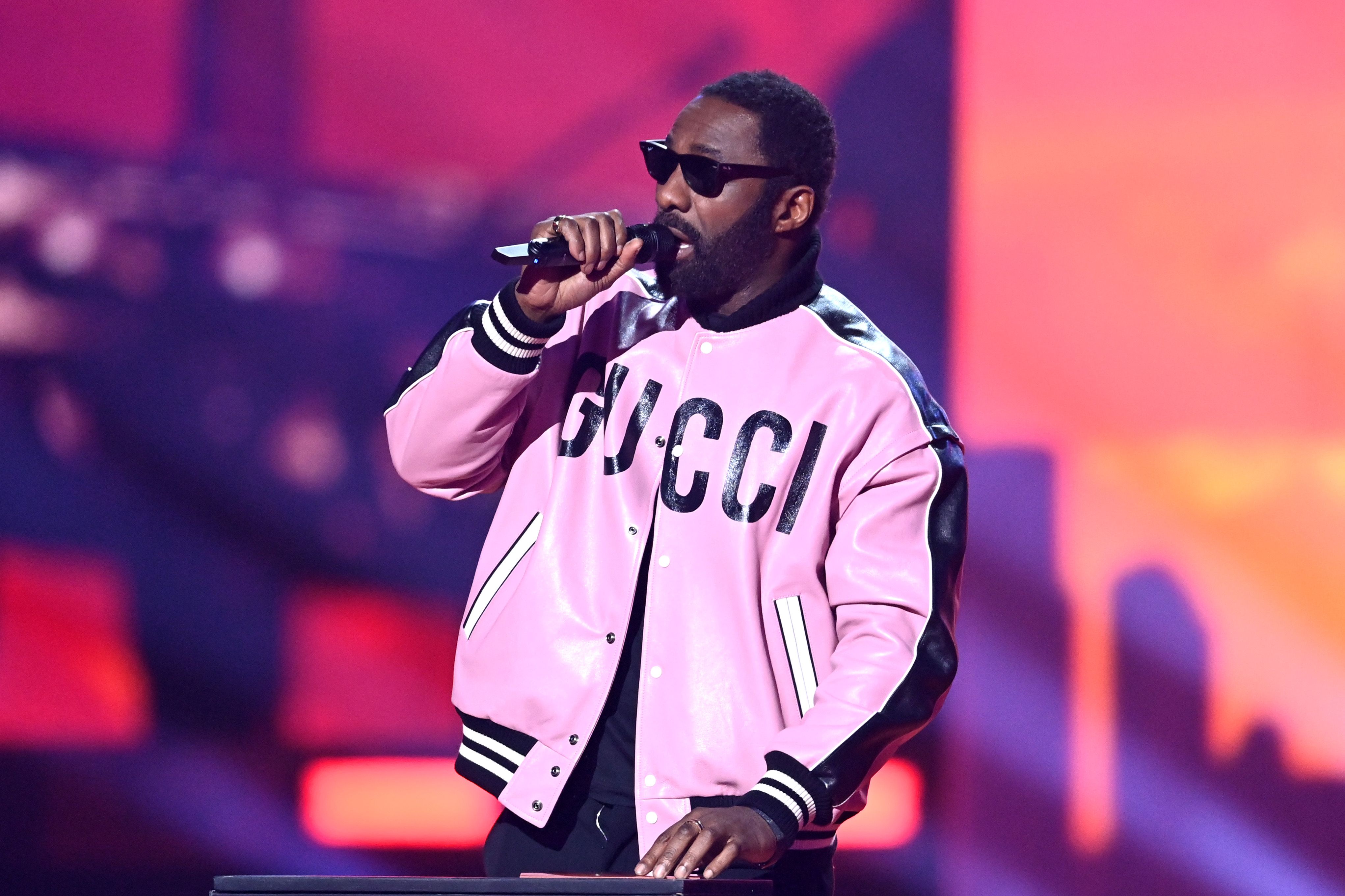 Idris Elba holds a microphone onstage during The BRIT Awards 2022