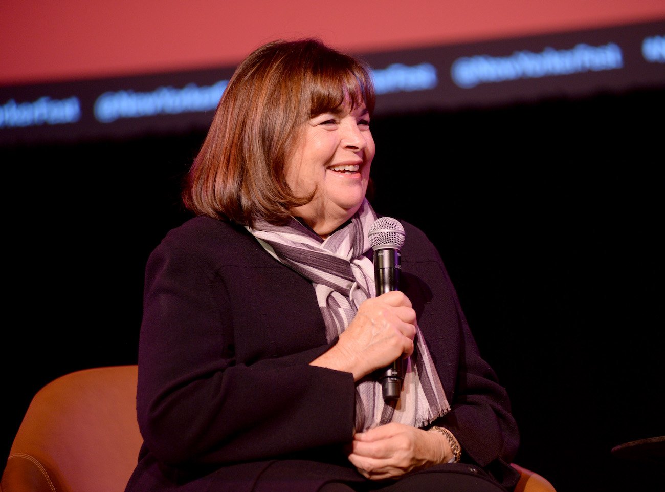 Ina Garten speaks into a microphone wearing a black top and scarf