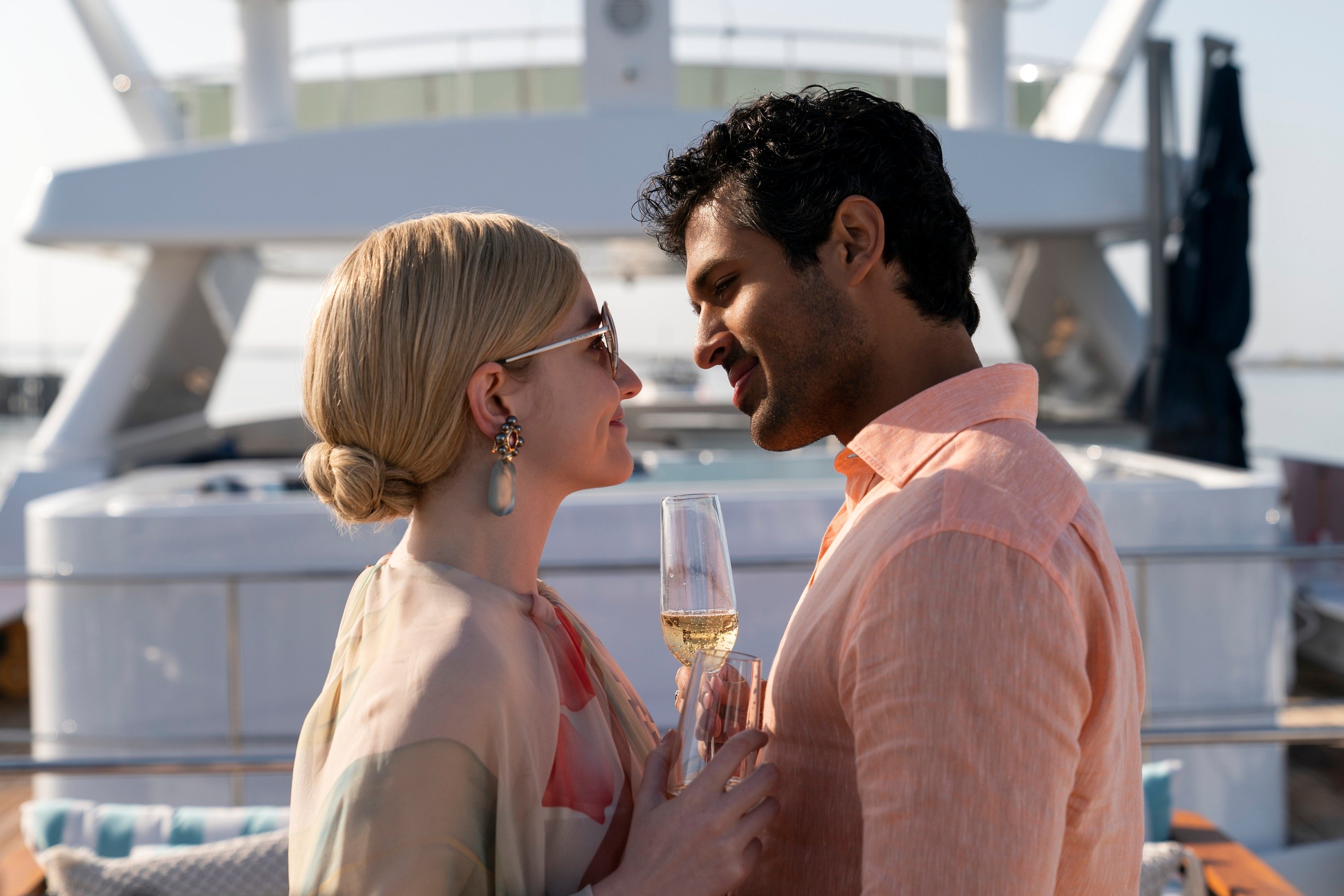 'Inventing Anna' Julia Garner and Saamer Usmani play Anna Delvey and Chase Sikorski about to kiss each other over a glass of champagne