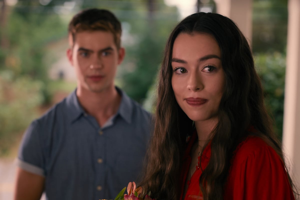 Annie, wearing a red shirt, looking at the camera, with Jackson in the background in 'Sweet Magnolias' Season 2