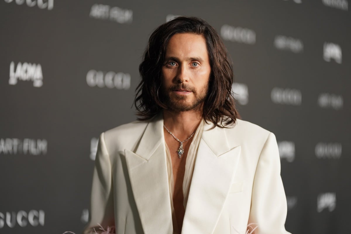 Jared Leto smirking while wearing a white suit.
